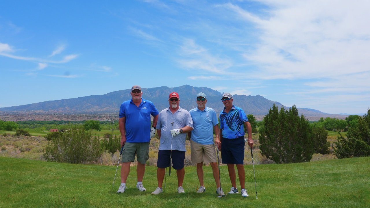 Four golfers at Sandia Golf Club with the Sandia Mountains behind them